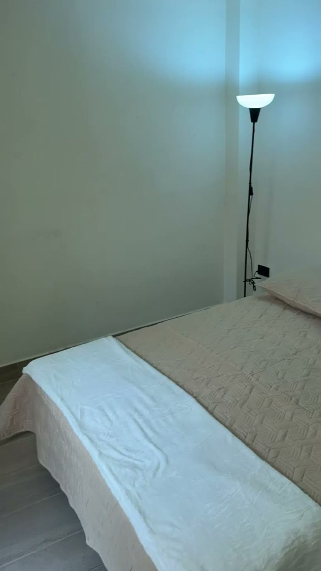 Alcoba pequeña con cama beige y lámpara de pie